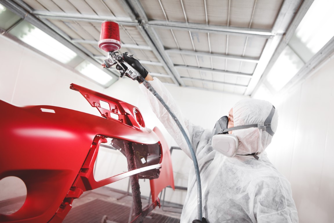 Auto mechanic worker painting car element with spray gun in a paint chamber during repair work. Service for repair restoration of the car.